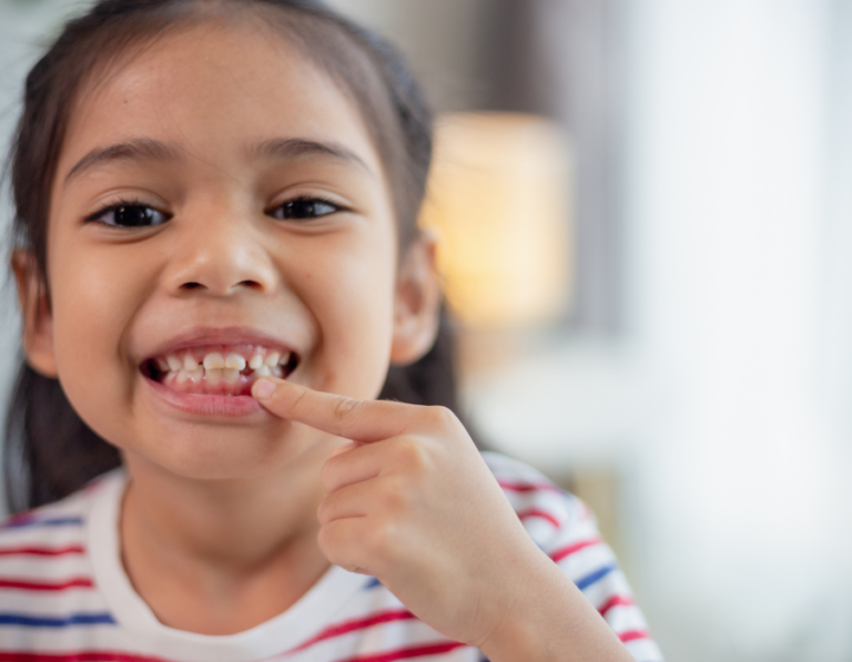 a little girl smiling and pointing at her teeth that are coming in