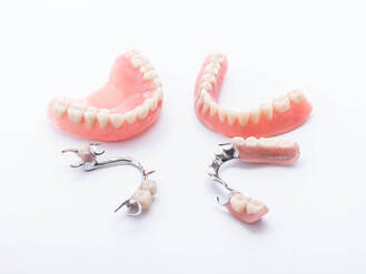 Four dental prosthetic devices displayed on white surface, including full upper and lower dentures with pink acrylic and artificial teeth, plus two partial dentures with metal frameworks and attached teeth.